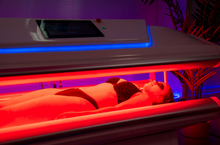 Load image into Gallery viewer, Person lying on a red light therapy bed with a digital display.